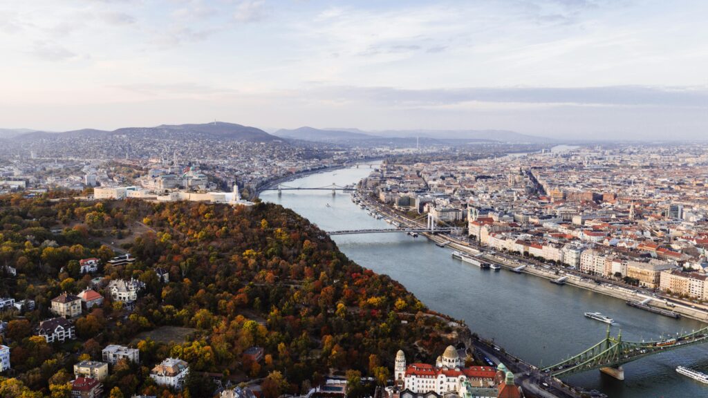 A stunning aerial view of Budapest showing the Danube River and iconic bridges with autumn foliage.